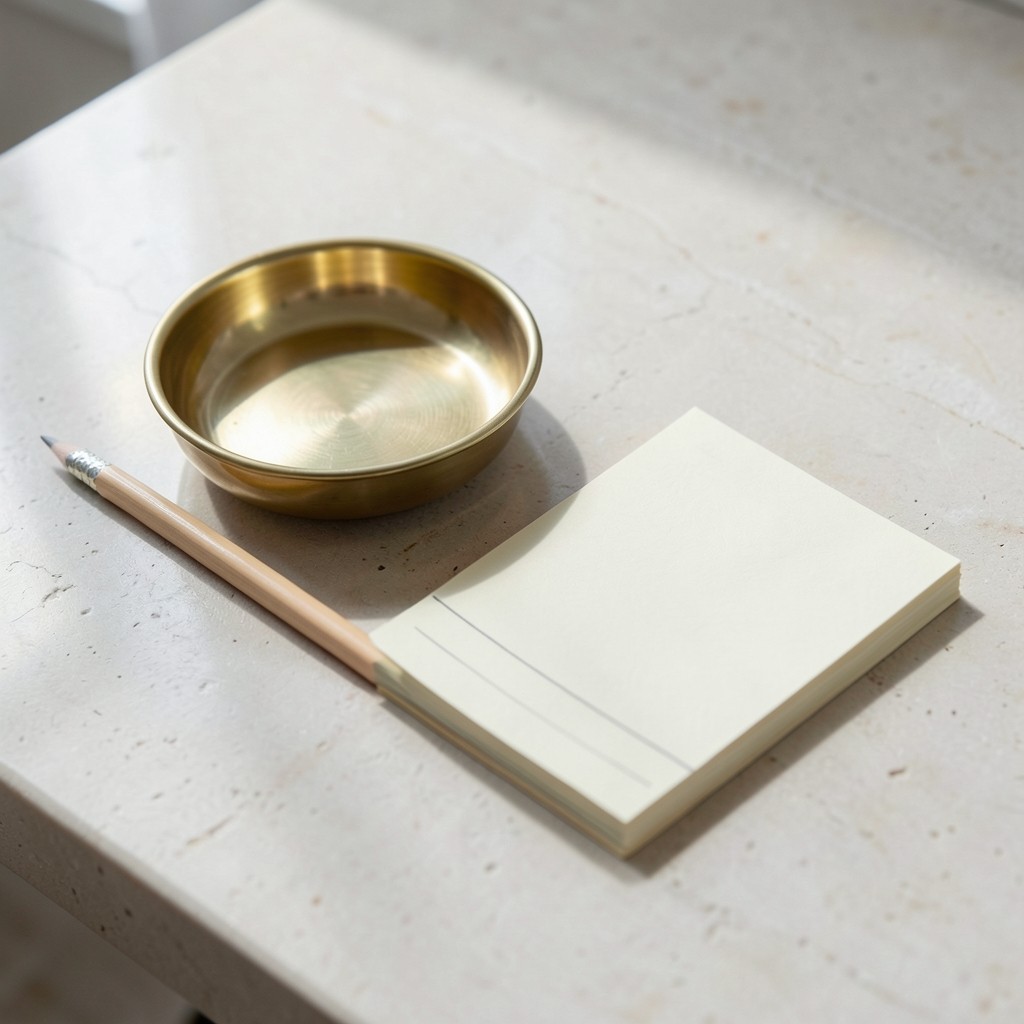 A brass dish, a pencil, and a blank pad on a stone table